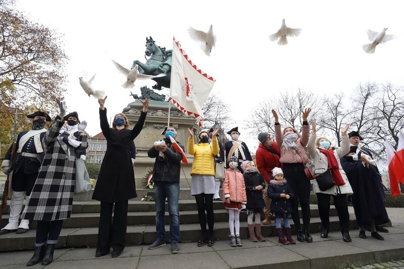 Grypa osób wypuszsza gołębie, z tyłu pomnik Jana Sobieskiego