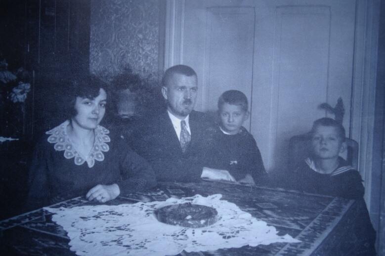 rodzina siedzi przy stole: matka, ojciec - na kolanach starszy syn, obok młodszy, czarno białe zdjęcie