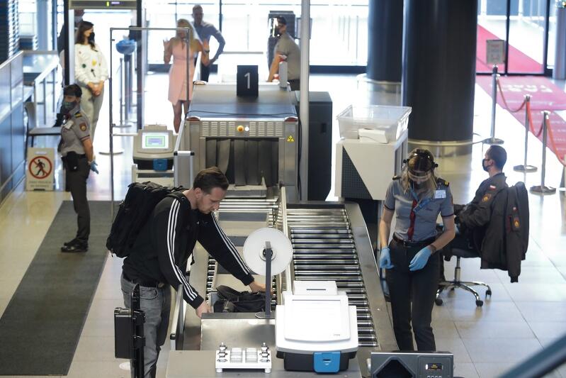 scena z odprawy na lotnisku, pracowniczka straży granicznej z twarzą zasłoniętą przyłbicą, pasażer z odkrytą twarzą, ludzie w tle