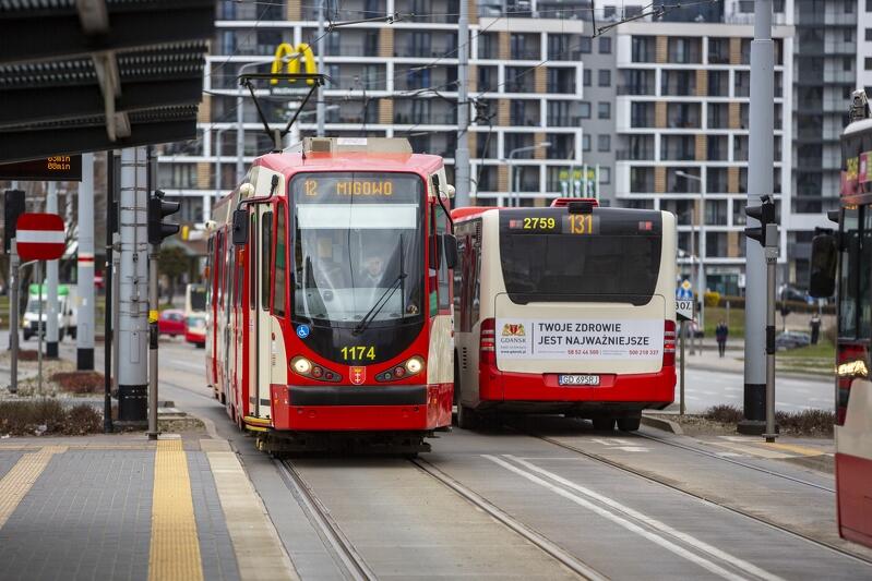 na zdjęciu biało-czerwony tramwaj mija się z kremowo-czerwonym autobusem miejskim, w tle widać wysoki budynek mieszkaniowy