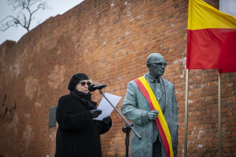 Krystyna Zachwatowicz-Wajda stoi obok pomnika, po jego lewej stronie, i czyta z kartki do mikrofonu przygotowany tekst krótkiego przemówienia