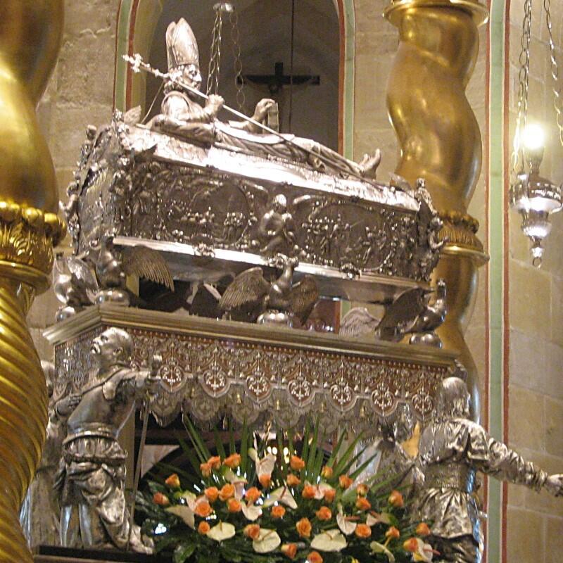 Widok relikwiarza: ozdobna trumienka w srebrnym kolorze, na jej wieku półleżąca postać biskupa - w mitrze, z pastorałem. U dołu, po bokach dwie również srebrne postaci rycerzy pilnujących relikwii