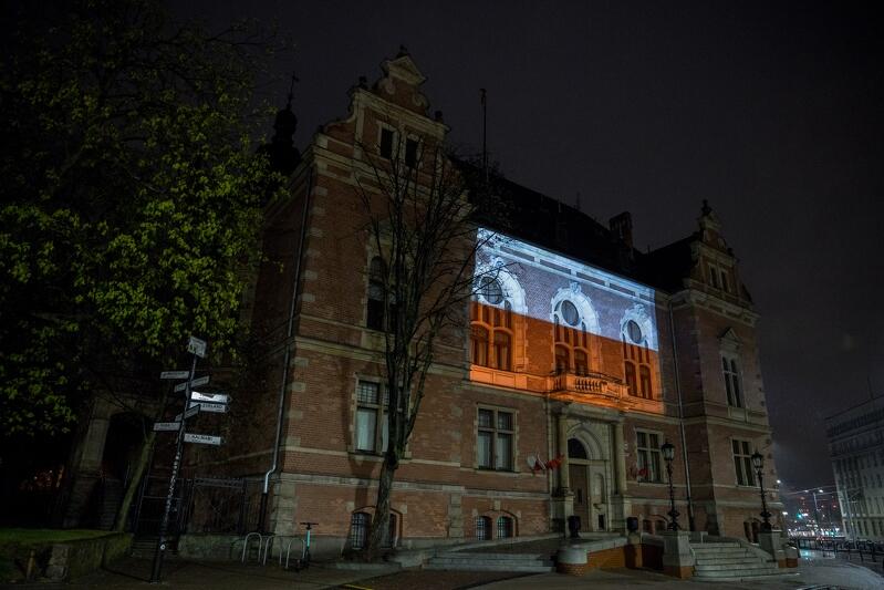 Budynek Nowego Ratusza (siedziba Rady Miasta Gdańska) wieczorową porą. Ciemno. Na budynku iluminacja biało-czerwonej flagi 