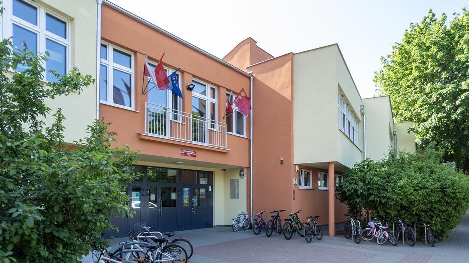 Budynek szkolny, przed którym zaparkowano kilka rowerów, a na fasadzie powieszono flagi Gdańska, Polski oraz Unii Europejskiej