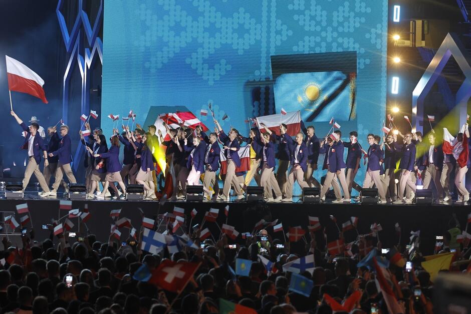 ponad 30 osób wchodzi na scenę, głównie młode kobiety i mężczyźni, niosą flagi Polski